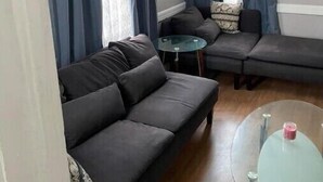 Uma sala de estar com um sofá de cor escura, uma mesa de centro de vidro e uma pequena mesa redonda.