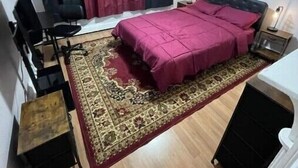 Quarto com cama, escrivaninha, cadeira, ventoinha no teto e janela com cortinas.