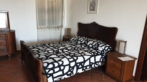 Une chambre à coucher comprenant un lit, une table de chevet, une commode, une fenêtre avec des rideaux et un tableau encadré accroché au mur.