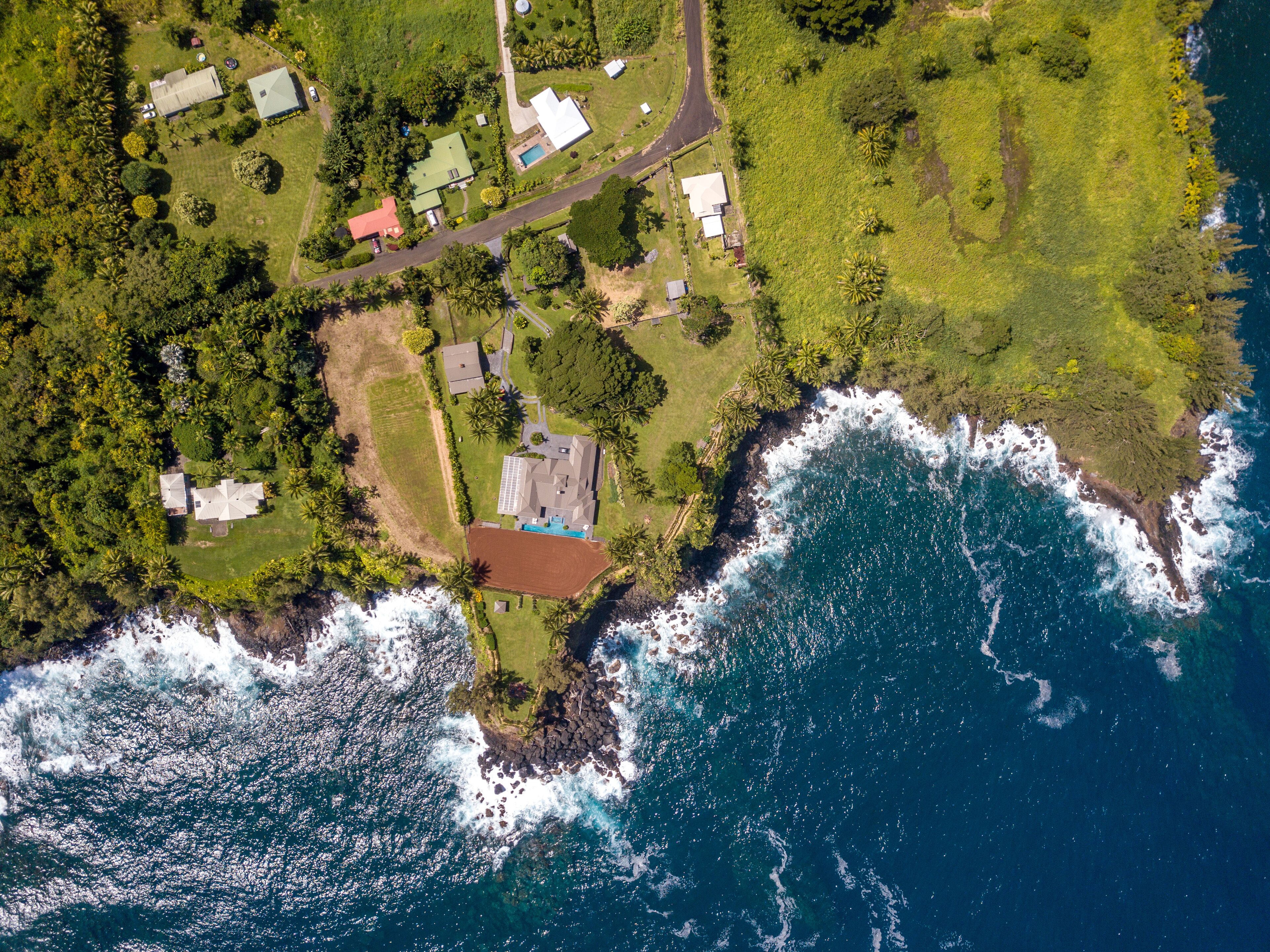 An aerial view of a coastal property with multiple buildings, a swimming pool, and a rocky shoreline.