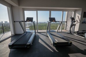 Une salle de sport équipée de deux tapis de course, dotée de grandes fenêtres et offrant une vue sur la ville.