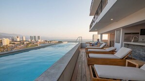 Una piscina en la azotea con sillones de descanso y vistas a la ciudad.