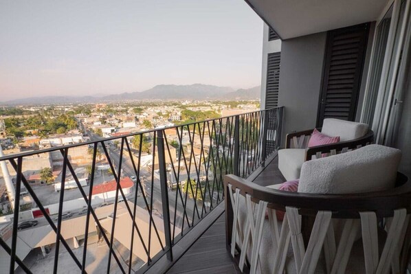Un balcon avec vue sur la ville et les montagnes. On y trouve une chaise avec des coussins.