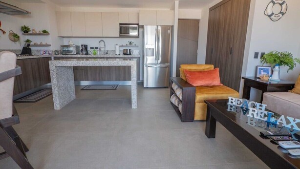 Una cocina moderna con una isla central, un comedor con sofá y una sala de estar con mesa de centro.