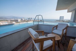 Un balcon doté de mobilier en bois, offrant une vue sur une piscine et le paysage urbain.