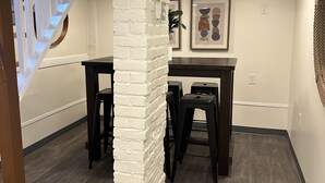 Un interno moderno con una colonna in mattoni bianchi, una scala con ringhiere bianche, un tavolo in legno scuro con degli sgabelli e un'opera d'arte incorniciata appesa al muro.