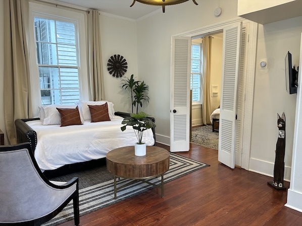 A bedroom with a bed, a potted plant, a round wooden table, and a chair.