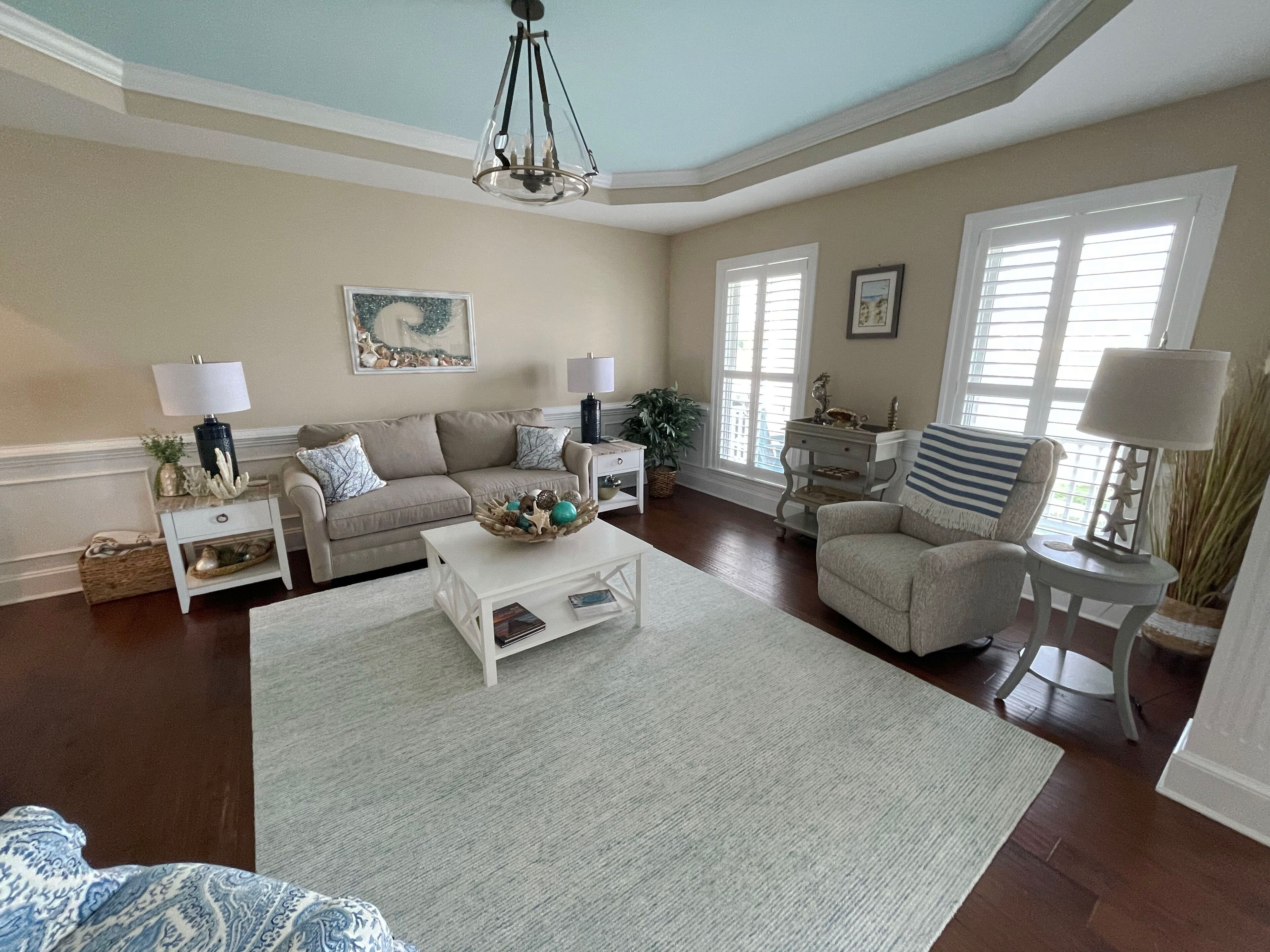 A spacious living room with a beige sofa, a white coffee table, and a patterned rug. There are two side tables with lamps and decorative items.