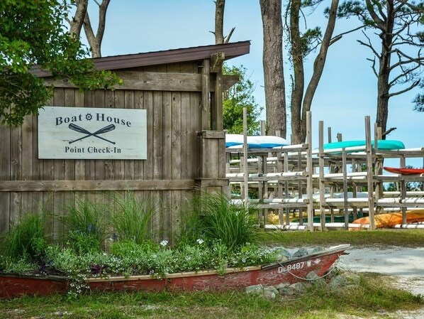A wooden structure labeled "Boat House Point Check-In" with a row of boats and a boat in the background.