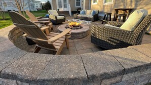 Une terrasse extérieure avec des fauteuils Adirondack, un foyer et des meubles en osier.