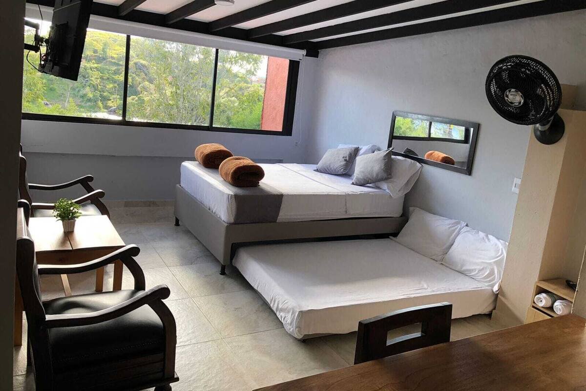 A compact bedroom with a bed, a desk, and a chair. There is a window with a view of greenery outside.