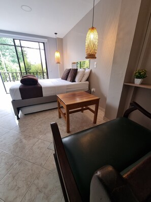 Un dormitorio moderno con cama, una mesa de madera, una silla y un balcón con vistas a zonas verdes.