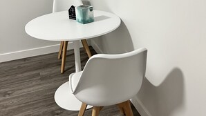 Une petite table ronde blanche, accompagnée de deux chaises blanches, une boîte de couleur turquoise posée sur la table et un plancher en bois.