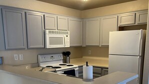 Una cocina con armarios blancos, un microondas, una estufa, un refrigerador y una pequeña isla con un lavamanos.