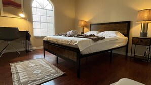 Un dormitorio con cama, lámparas de noche, escritorio y ventana con persianas.