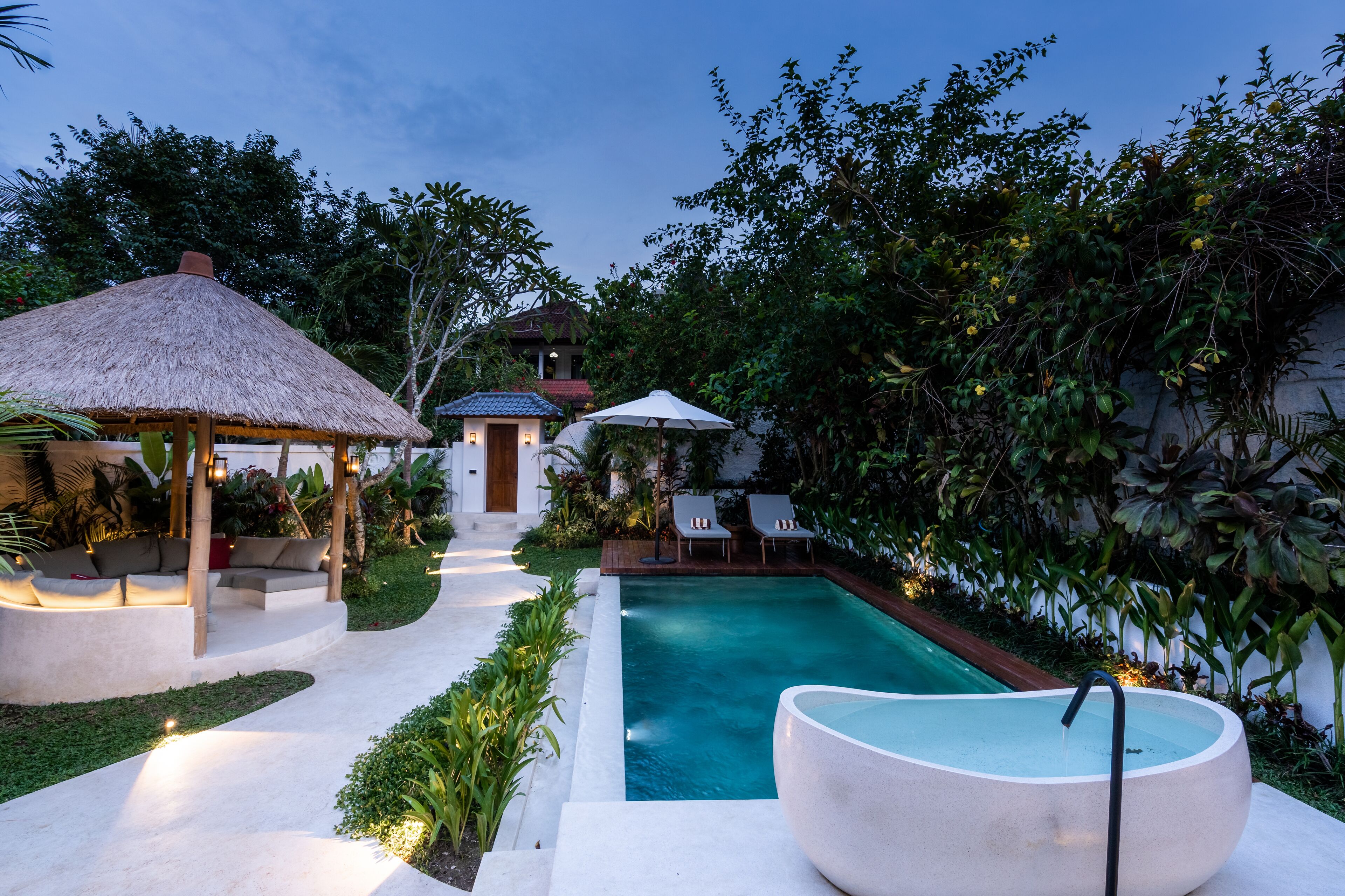 A pool area with a thatched-roof gazebo, lounge chairs, and a large bowl-shaped hot tub.