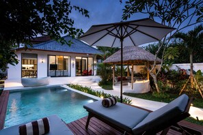 A modern house with a swimming pool, outdoor seating, and a thatched-roof structure.