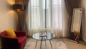A room with a red armchair, a round glass table, a floor lamp, a large mirror, and sheer curtains. - 2 Bed Apartment Sleeps 4 - Pool - Free Parking (Lekki 1)