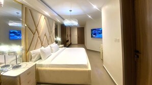 A modern hotel room with a large bed, a vanity with a mirror, and a television on the wall. - 2 Bed Apartment Sleeps 4 - Pool - Free Parking (Lekki 1)