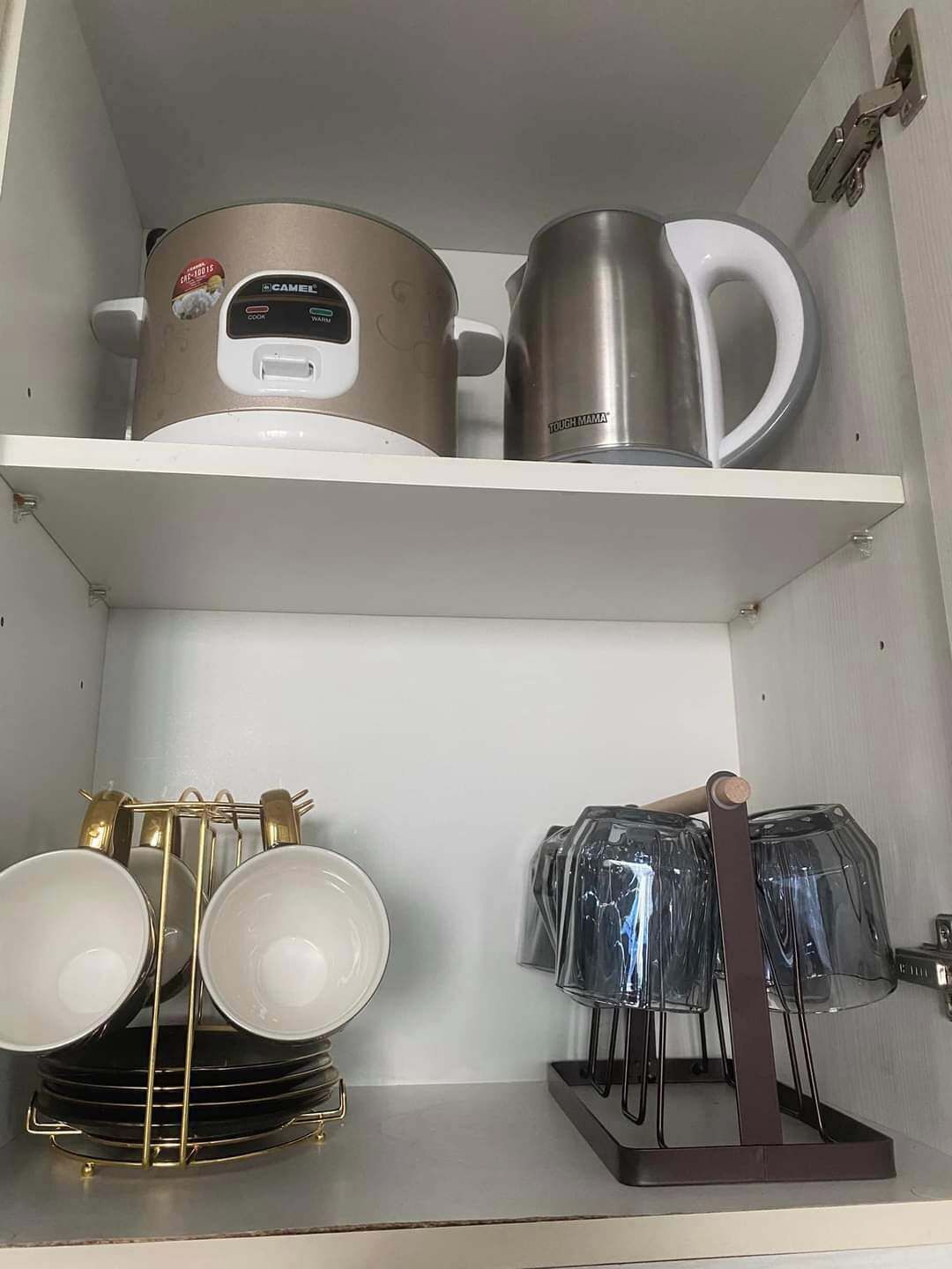 Une étagère de cuisine avec une machine à café, une bouilloire et une tasse. En dessous, on trouve une pile d'assiettes et un porte-verres.