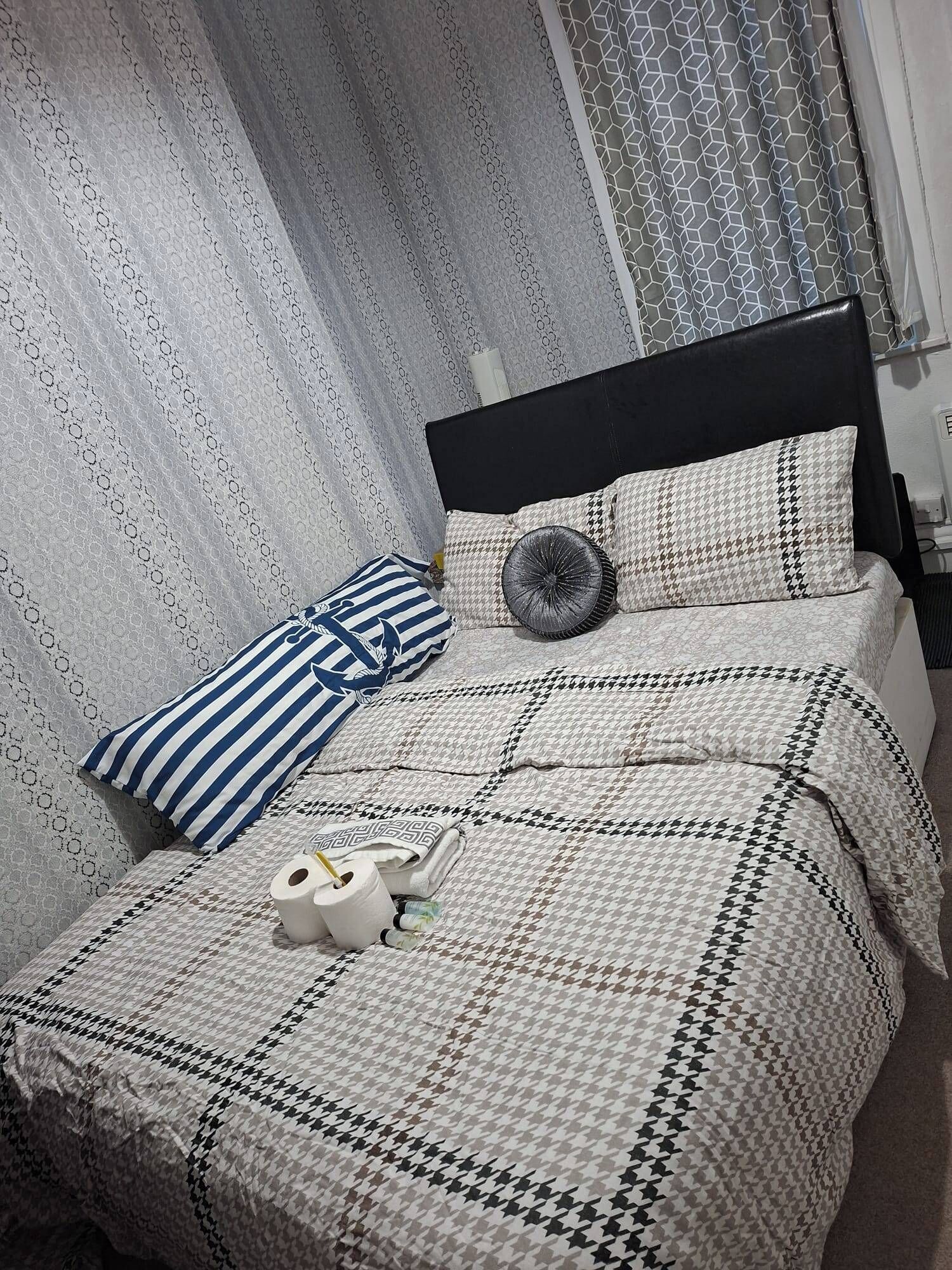 A neatly made bed with a patterned bedspread, two pillows, a decorative pillow, and a rolled-up towel.