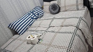Ein ordentlich bezogenes Bett mit einer gemusterten Tagesdecke, zwei Kissen und einem Zierkissen, sowie ein aufgerolltes Handtuch.