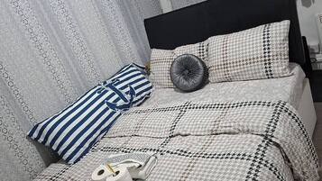 A neatly made bed with a patterned bedspread, two pillows, a decorative pillow, and a rolled-up towel.