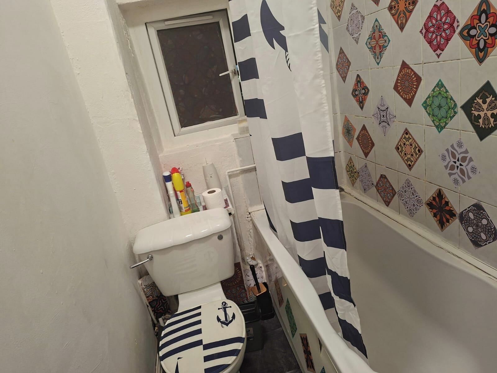 A small bathroom with a toilet, a window, and a shower curtain.