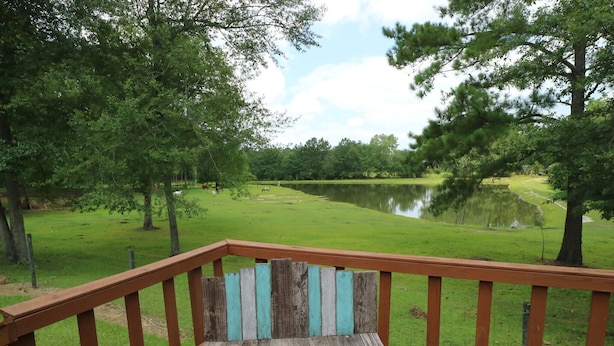 A wooden deck with a bench overlooking a grassy area and a body of water.