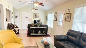 A living room with a brown leather sofa, a yellow armchair, a coffee table, and a fireplace. There are two doors, a ceiling fan, and a window with blinds.