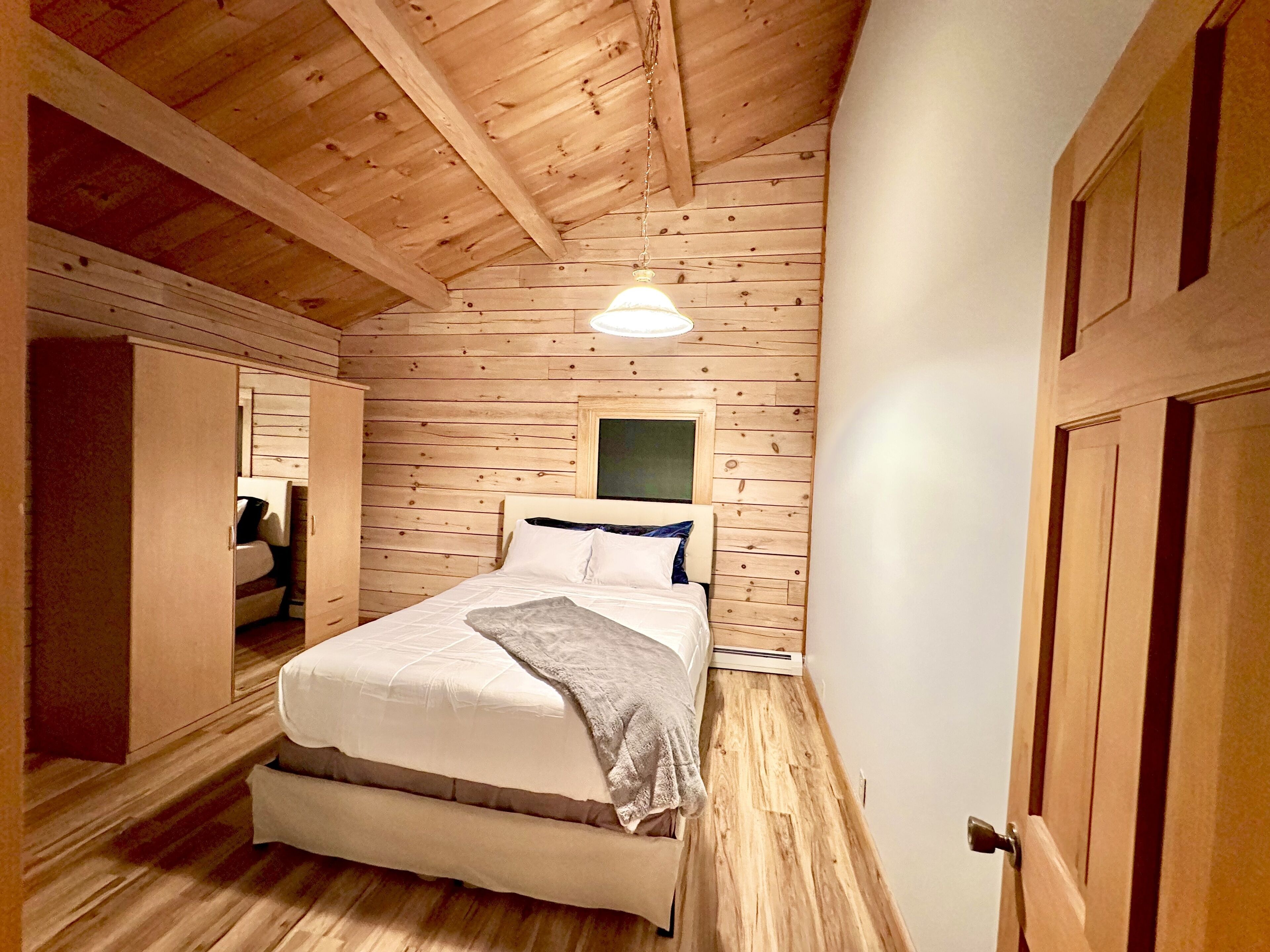 Een slaapkamer met een houten plafond, een bed met witte beddengoed, een nachtkastje en een nachttafel.