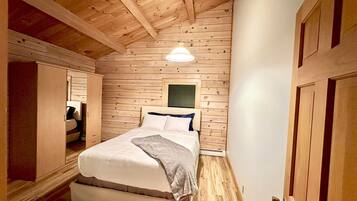 Een slaapkamer met een houten plafond, een bed met witte beddengoed, een nachtkastje en een nachttafel.