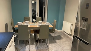 A modern kitchen with a dining area, featuring a stainless steel refrigerator, a dining table set with plates and glasses, and chairs. - MK439FJ Sleeps 7 with Pet Friendly Garden (Bedford)