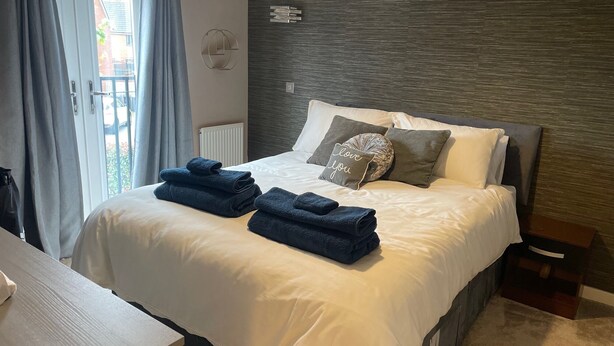 A neatly made bed with white and grey linens, two folded blue towels, and a pillow with "love you" text. - MK439FJ Sleeps 7 with Pet Friendly Garden (Bedford)