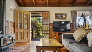 A cozy living room with a wooden table, a sofa, a television, and a door leading to a balcony.