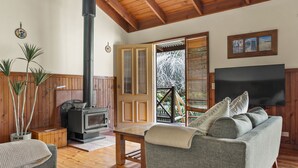 A cozy living room with a fireplace, wooden ceiling beams, a sofa, and a television.