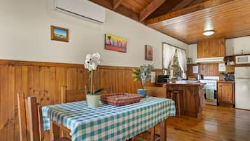 A wooden interior with a dining table covered by a checkered tablecloth, wooden chairs, a kitchen area with wooden cabinets, and a microwave.