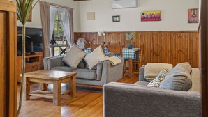 A cozy living room with a wooden ceiling, a television, a sofa, and a dining table.