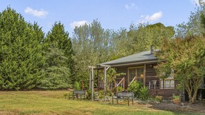 A rustic cabin with a porch, surrounded by dense trees and a grassy yard.