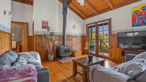 A cozy living room with wooden floors, a fireplace, a ceiling fan, and a television.