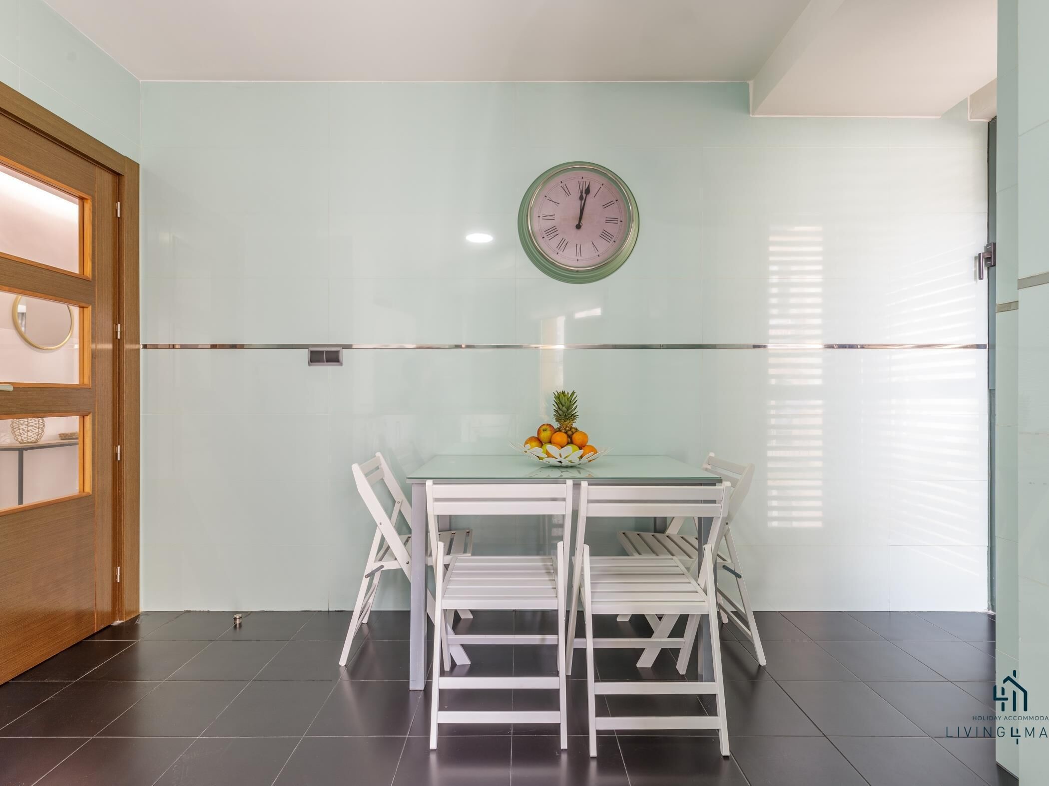 A dining area with a glass table, white chairs, and a clock on the wall.