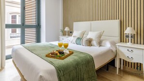 A modern hotel room with a large bed, a wooden slatted wall, a nightstand with a lamp, and a window with blinds.