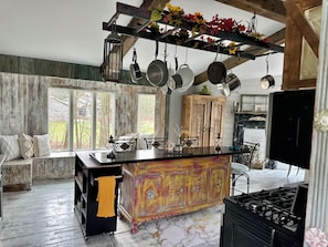 Cozinha com bancada de mármore, panelas penduradas, armário de madeira e janela com vista.