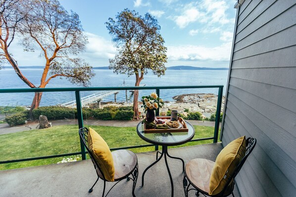 Un balcon avec une table, deux chaises, un vase de fleurs et un plateau contenant des biscuits et une tasse.