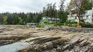 Un hotel frente al mar con costa rocosa, un puente y un paisaje boscoso de fondo.