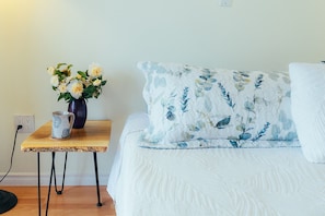 A bedroom with a bed, a nightstand, a vase with flowers, and a lamp. - Beach Bliss oceanfront king studio! Balcony, stunning view, pool, dock & hot tub (Ladysmith)