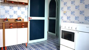 A kitchen with a blue and white tiled backsplash, a white stove, and a door with a red handle. - Nami Holiday Home for six Guests With Outdoor Space (Melendugno)