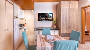 A modern kitchen with white cabinets, a wooden ceiling, and a flat-screen TV mounted above a dining table with chairs. - Studio Apartment Iva Rijeka Suburbs, Rijeka, Croatia (Rijeka)
