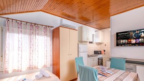 A room with a bed, a table with chairs, a kitchen area, and a wall-mounted TV displaying a movie. - Studio Apartment Iva Rijeka Suburbs, Rijeka, Croatia (Rijeka)