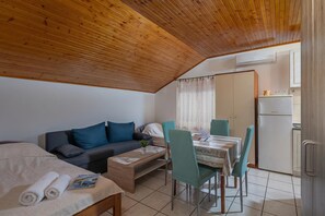 A compact room with a wooden ceiling, a sofa, a dining table with chairs, a bed, and a kitchenette. - Studio Apartment Iva, Rijeka, Croatia (Rijeka)